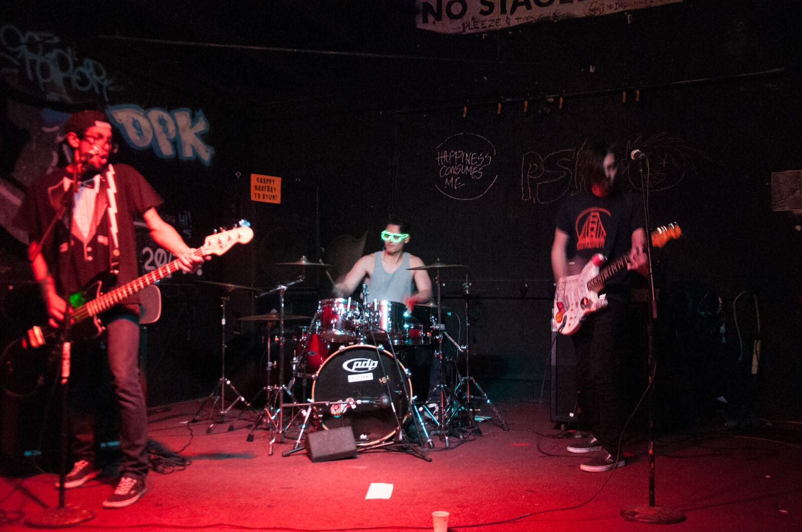 Small punk band performing in a black-room venue with red stage wash